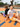 Two players sitting back to back on an orange court in Rival shorts